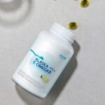 Atomy Alaska E-Omega3 bottle lying down on a textured background with scattered softgels